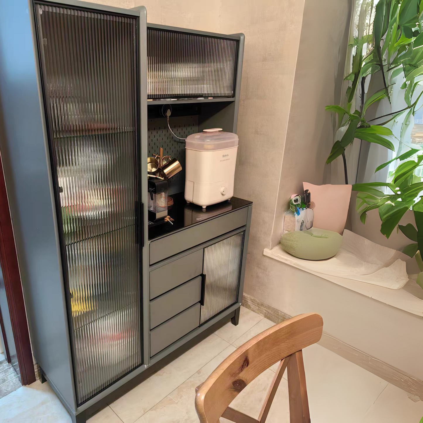 Cabinet with glass doors in a room with a plant and a chair.